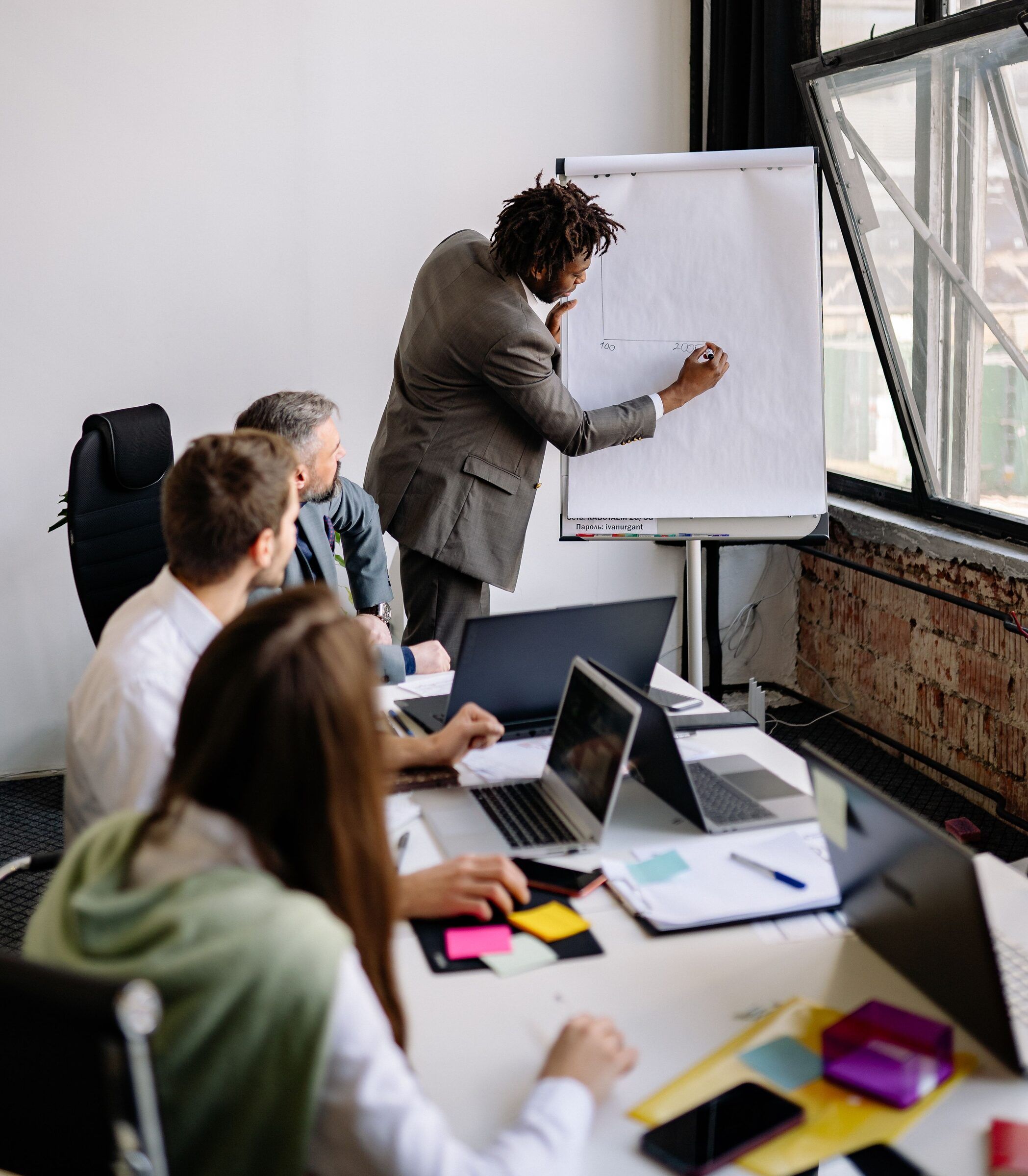 A small group gathers around a flip chart in a meeting room, working through a problem together.